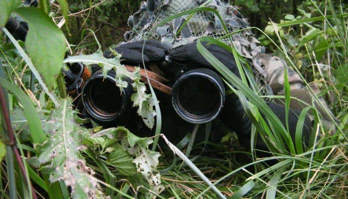 Surveillance Agent disguised in a ghillie suit looking through binoculars