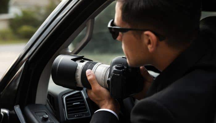 Surveillance agent holding a camera with a very long lens attempting to take a picture of the target while in his car.