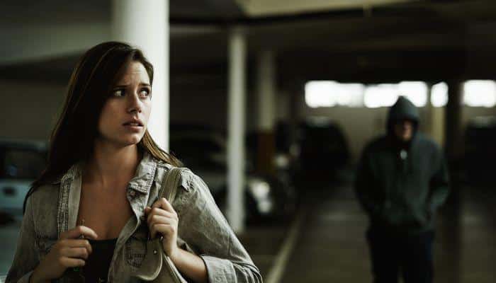A woman in a parking garage practicing situational awareness observing the hooded figure following her.